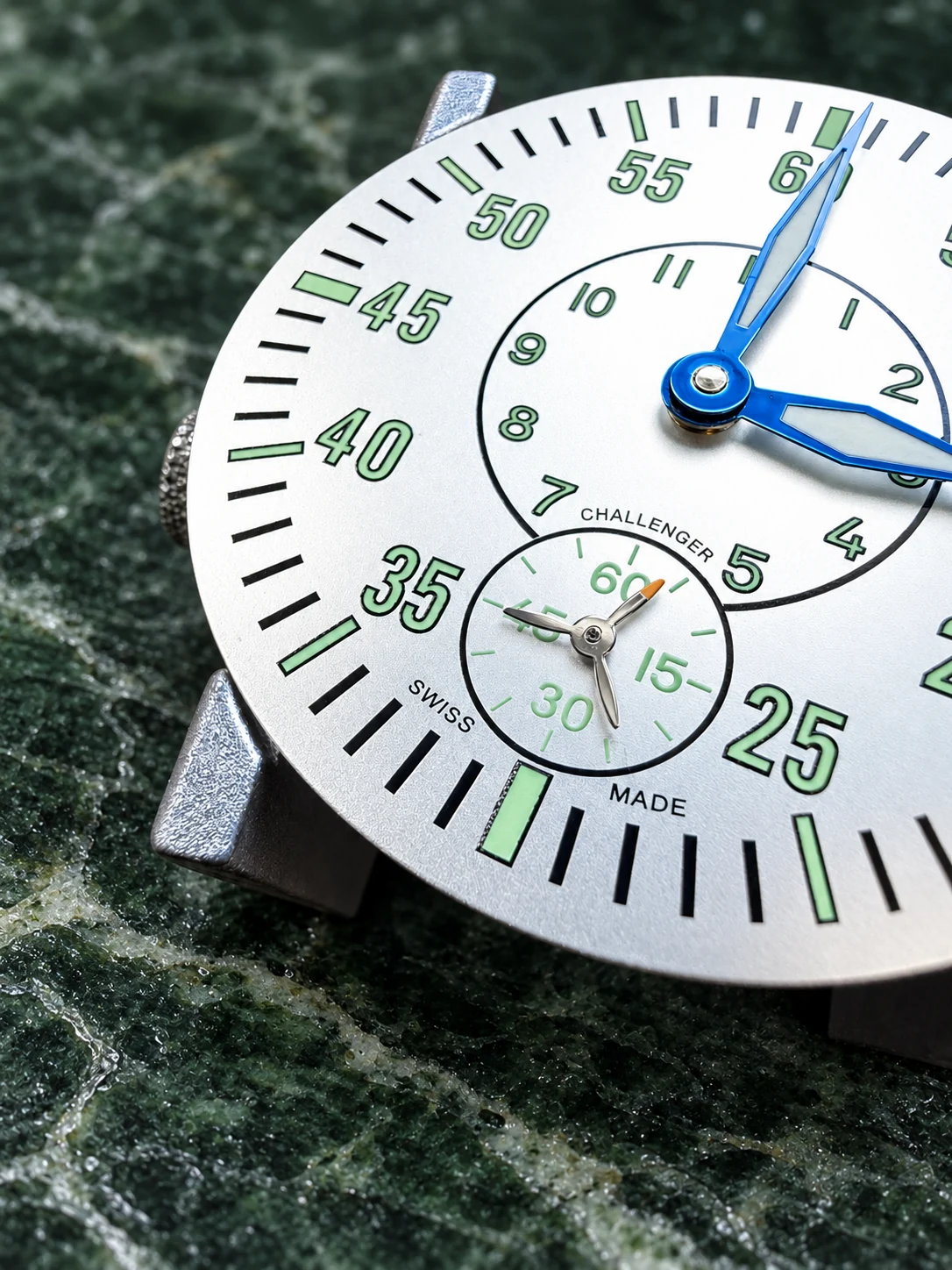A white watch dial with blue hands on forest green stone
